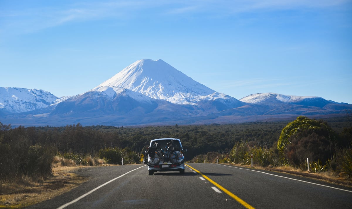 A modern car driving toward snow-capped mountains on a clear day